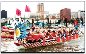 Kaohsiung Dragon Boat Race in Portland A dragon boat team rowing through the water in front of Portland's city skyline during a festival.