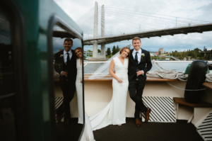 Wedding couple on bow of Willamette Star shown in reflection in the window with Tillikum Bridge in background